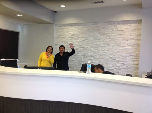 Front desk of a Dental office with two employees waving at the camera.