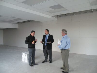 Three men standing in a large empty room of a building.