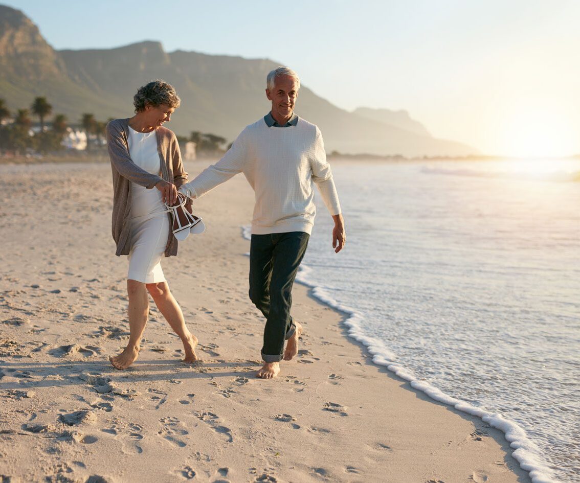 Mature couple walking along the beach waters.